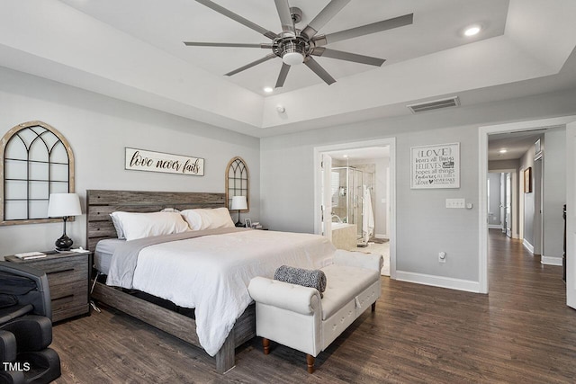 bedroom with ceiling fan, dark hardwood / wood-style flooring, ensuite bathroom, and a tray ceiling