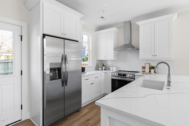 kitchen with light stone counters, wall chimney exhaust hood, white cabinets, appliances with stainless steel finishes, and sink