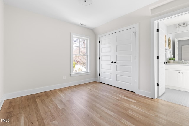 unfurnished bedroom featuring a closet, light hardwood / wood-style floors, sink, ensuite bathroom, and lofted ceiling