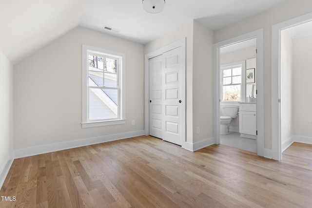 unfurnished bedroom featuring a closet, multiple windows, vaulted ceiling, and light wood-type flooring