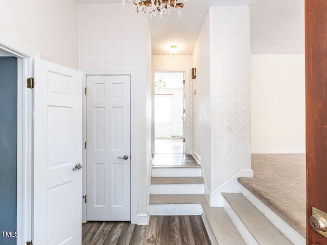 corridor with dark wood-type flooring and an inviting chandelier