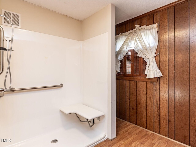 bathroom with a shower, wooden walls, and hardwood / wood-style flooring