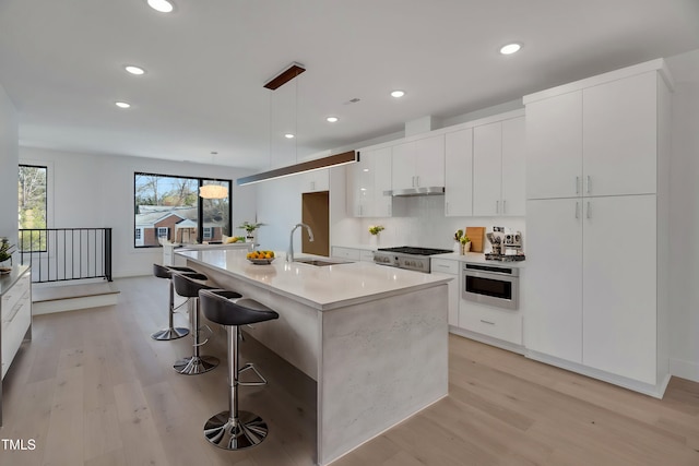 kitchen with sink, light hardwood / wood-style flooring, a kitchen island with sink, hanging light fixtures, and white cabinets