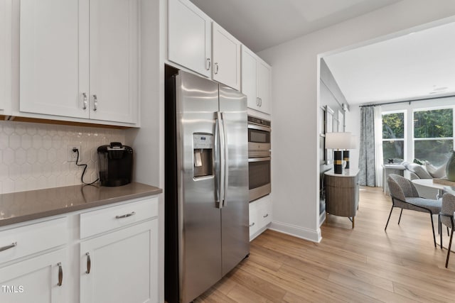 kitchen featuring stainless steel appliances, white cabinets, decorative backsplash, and light hardwood / wood-style floors