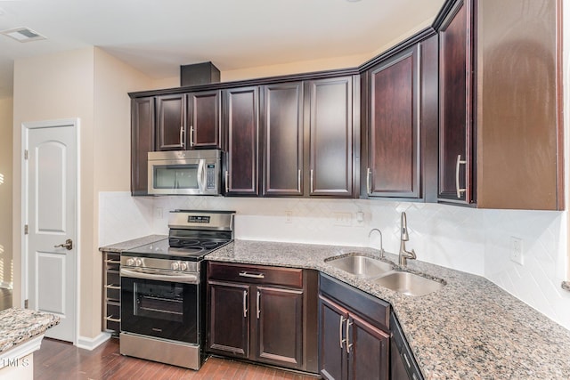 kitchen with sink, appliances with stainless steel finishes, dark brown cabinets, dark hardwood / wood-style floors, and light stone counters