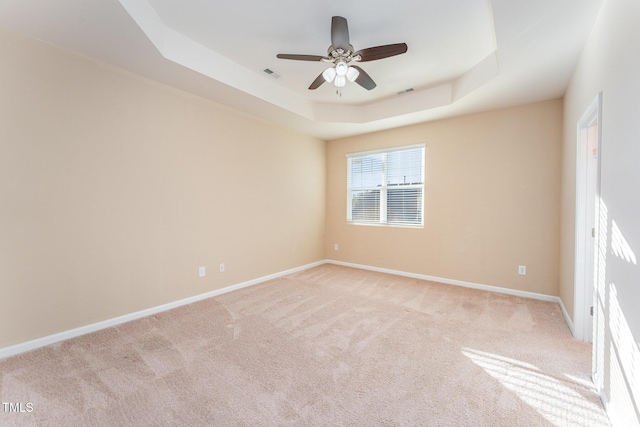 spare room featuring light carpet, ceiling fan, and a tray ceiling