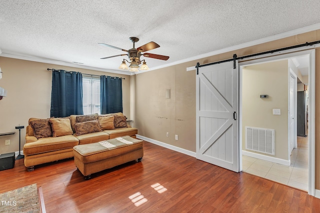 living room with ceiling fan, crown molding, a barn door, and hardwood / wood-style flooring