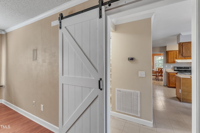 corridor featuring a barn door, crown molding, and a textured ceiling