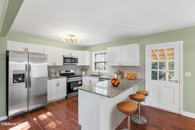 kitchen with appliances with stainless steel finishes, white cabinetry, sink, a kitchen bar, and kitchen peninsula