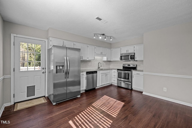 kitchen with appliances with stainless steel finishes, white cabinetry, sink, backsplash, and dark wood-type flooring