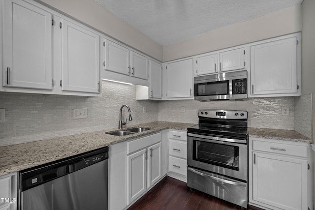 kitchen with sink, stainless steel appliances, tasteful backsplash, light stone countertops, and white cabinets