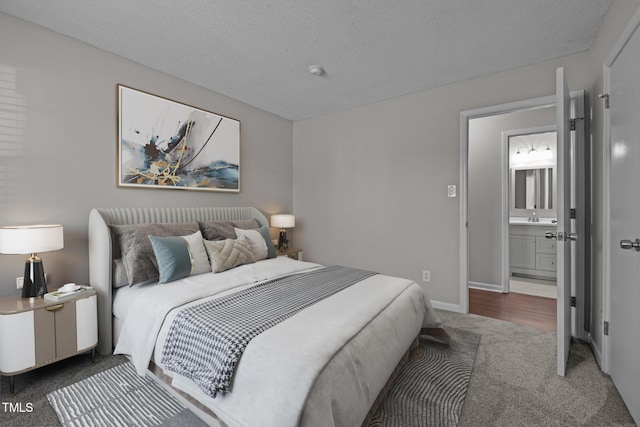 bedroom featuring sink, ensuite bath, a textured ceiling, and dark colored carpet