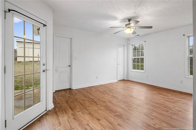 empty room featuring a textured ceiling, ceiling fan, light hardwood / wood-style floors, and plenty of natural light