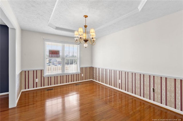 empty room with a notable chandelier, a raised ceiling, a textured ceiling, and wood-type flooring