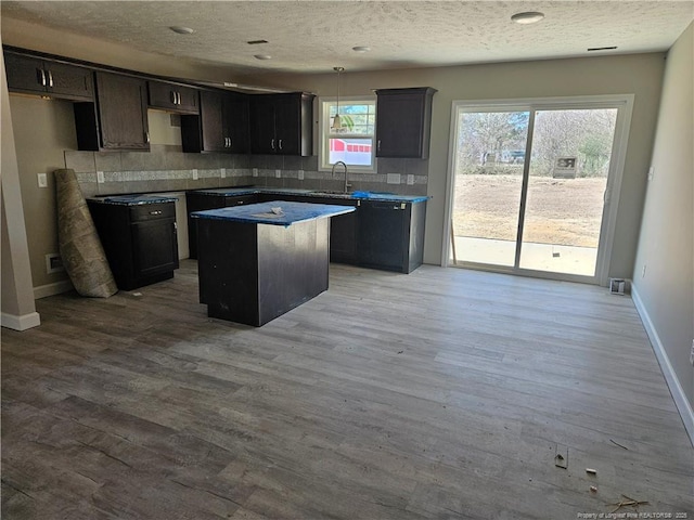 kitchen featuring a center island, decorative backsplash, a sink, wood finished floors, and baseboards