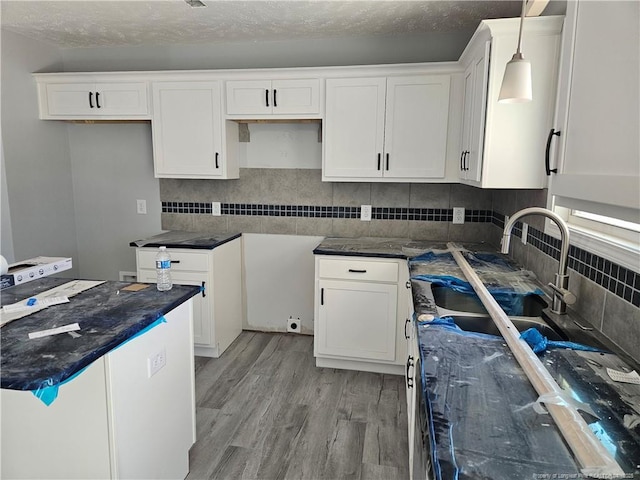 kitchen with tasteful backsplash, light wood-type flooring, white cabinets, and hanging light fixtures