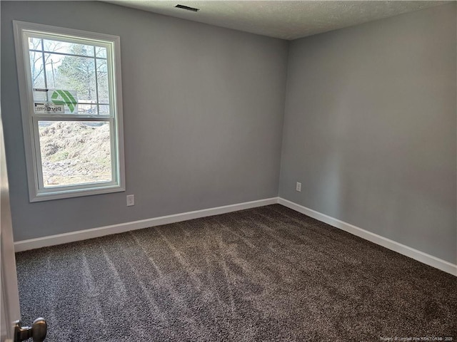 spare room featuring visible vents, baseboards, dark colored carpet, and a textured ceiling