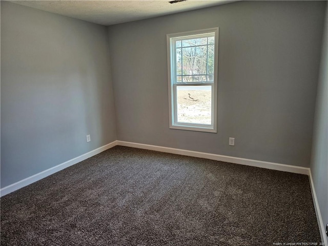 empty room featuring visible vents, dark carpet, and baseboards