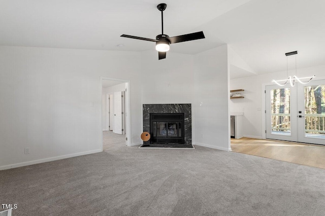 unfurnished living room featuring light carpet, a high end fireplace, lofted ceiling, and ceiling fan with notable chandelier