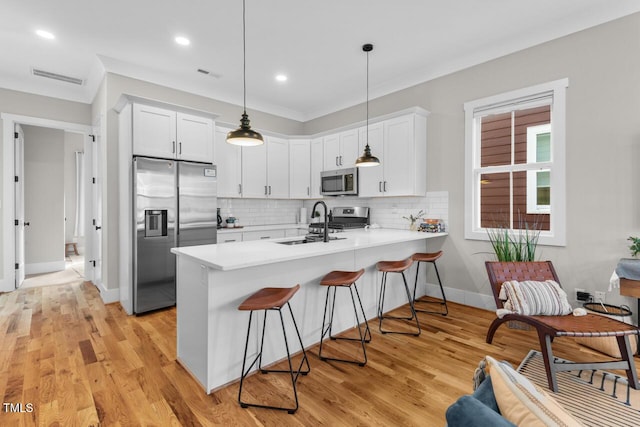 kitchen featuring pendant lighting, appliances with stainless steel finishes, kitchen peninsula, and white cabinets