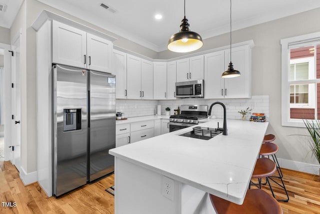 kitchen featuring white cabinetry, a kitchen bar, hanging light fixtures, and appliances with stainless steel finishes