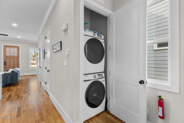 laundry area with crown molding, stacked washer and clothes dryer, and light hardwood / wood-style flooring