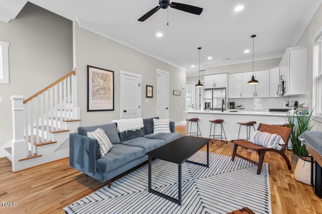 living room featuring ceiling fan, ornamental molding, sink, and light hardwood / wood-style floors