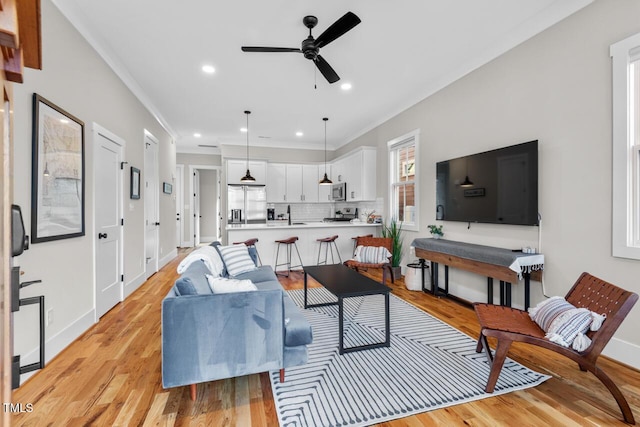 living room featuring ornamental molding, sink, ceiling fan, and light wood-type flooring