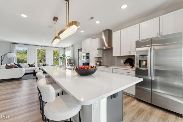 kitchen featuring appliances with stainless steel finishes, an island with sink, white cabinets, and wall chimney exhaust hood