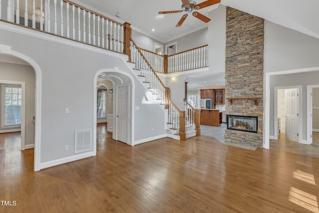 unfurnished living room featuring light hardwood / wood-style flooring, a towering ceiling, a fireplace, and ceiling fan