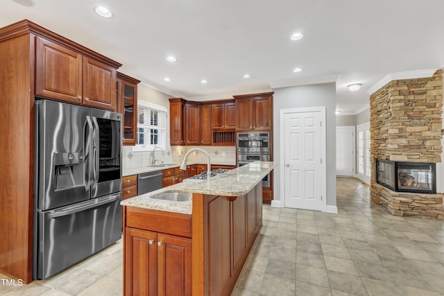 kitchen with light stone counters, a center island with sink, stainless steel appliances, a fireplace, and decorative backsplash