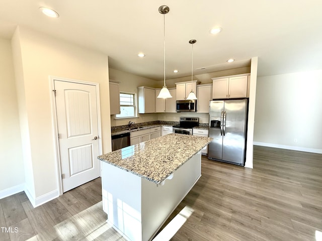 kitchen with light stone counters, light hardwood / wood-style flooring, decorative light fixtures, a kitchen island, and appliances with stainless steel finishes