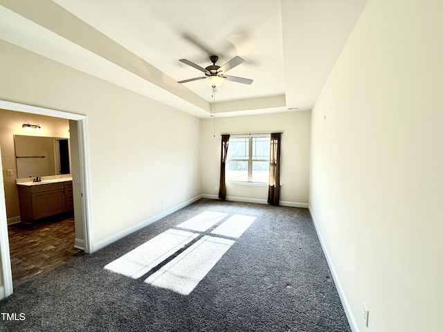 spare room with a raised ceiling, ceiling fan, dark carpet, and sink