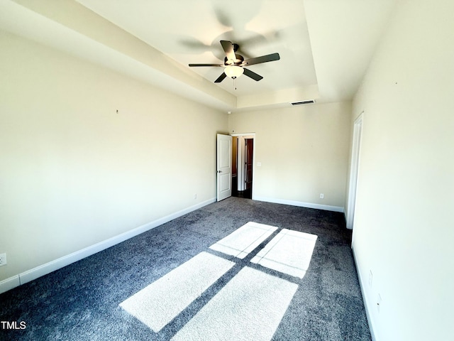 unfurnished bedroom with ceiling fan, dark colored carpet, and a tray ceiling