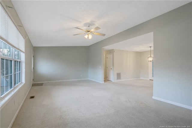 unfurnished room with ceiling fan with notable chandelier, light colored carpet, and plenty of natural light