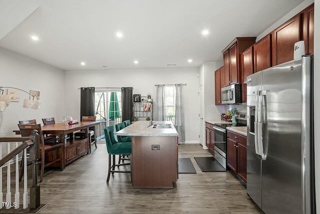 kitchen featuring a kitchen bar, dark wood-type flooring, appliances with stainless steel finishes, and a kitchen island with sink