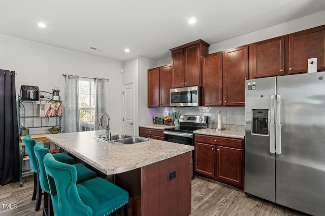 kitchen featuring light hardwood / wood-style floors, a kitchen bar, sink, a kitchen island with sink, and appliances with stainless steel finishes