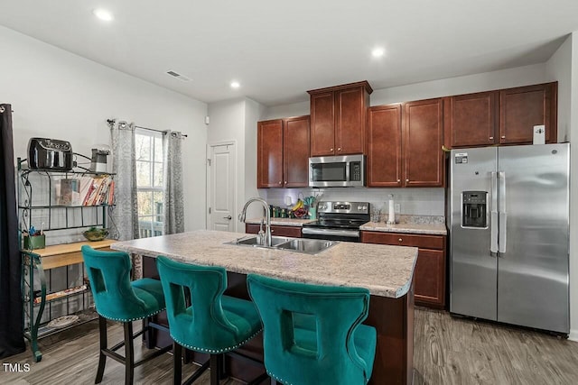 kitchen with sink, light hardwood / wood-style flooring, an island with sink, a kitchen breakfast bar, and stainless steel appliances