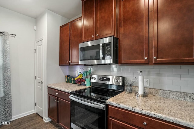 kitchen featuring tasteful backsplash, light stone countertops, appliances with stainless steel finishes, and dark wood-type flooring