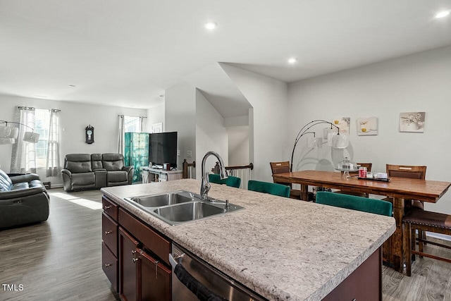 kitchen featuring an island with sink, stainless steel dishwasher, light hardwood / wood-style flooring, dark brown cabinetry, and sink