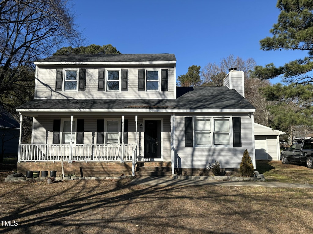 view of front of property featuring covered porch, a front lawn, a garage, and an outbuilding