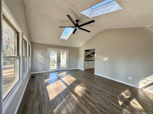 empty room with ceiling fan, dark wood-type flooring, french doors, lofted ceiling with skylight, and a textured ceiling