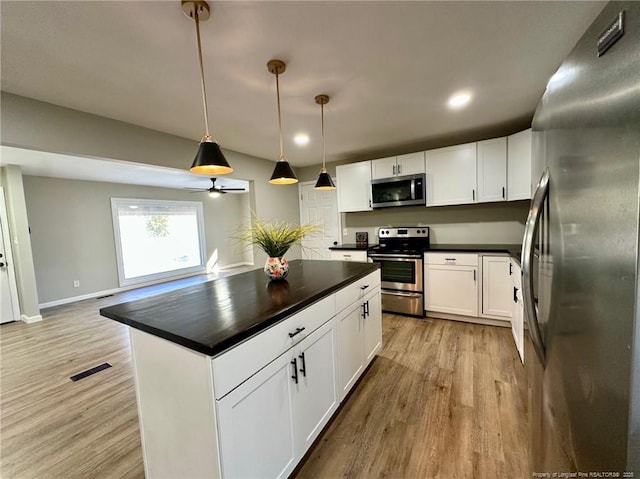 kitchen with white cabinets, light wood-type flooring, hanging light fixtures, a kitchen island, and appliances with stainless steel finishes