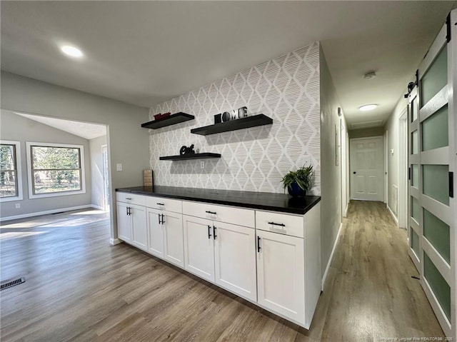 bar featuring lofted ceiling, white cabinetry, light wood-type flooring, and a barn door