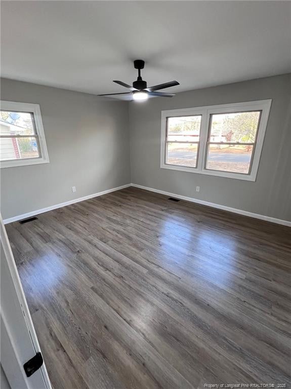 unfurnished room with a healthy amount of sunlight, dark wood-type flooring, and ceiling fan