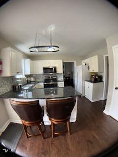 kitchen with dark countertops, a breakfast bar area, a peninsula, stainless steel appliances, and dark wood-style flooring