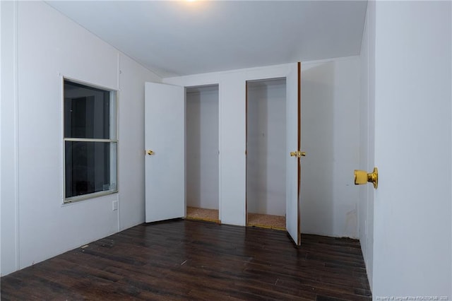 unfurnished bedroom featuring dark wood-type flooring and multiple closets