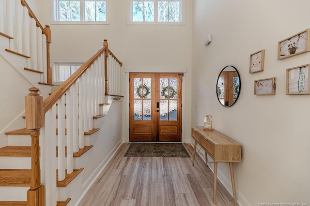 entrance foyer featuring french doors, light wood-type flooring, and a towering ceiling