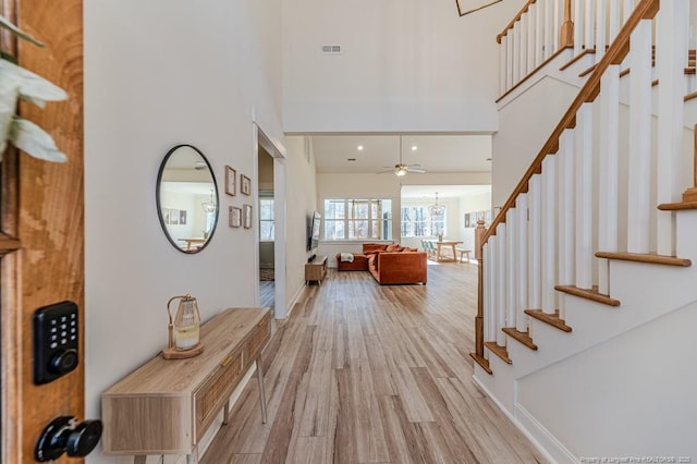 foyer entrance with a towering ceiling, ceiling fan, and light hardwood / wood-style flooring