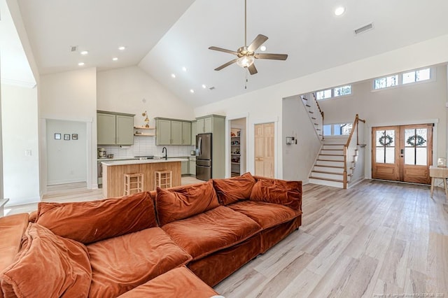 living room with ceiling fan, light hardwood / wood-style floors, french doors, and high vaulted ceiling